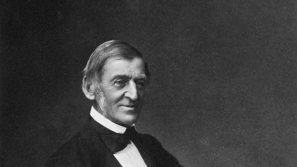 ralph waldo emerson sitting at a table and holding a book as he looks up