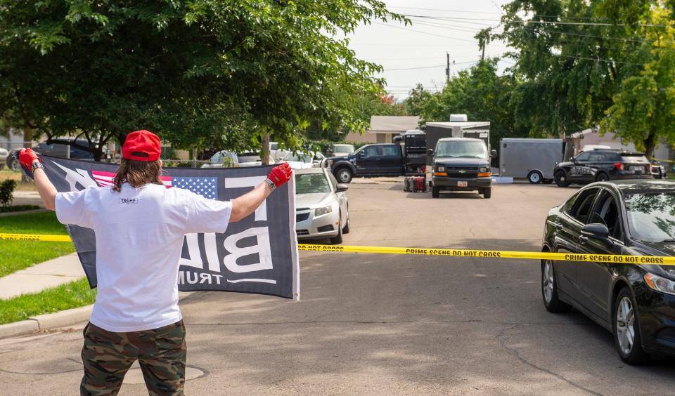 A man holds a flag as law enforcement officers investigate the home of Craig Deleeuw Robertson in Provo, Utah, Wednesday, Aug. 9, 2023.