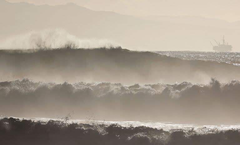 Grandes olas rompen cerca de la playa con una plataforma petrolera en la distancia el 28 de diciembre de 2023.