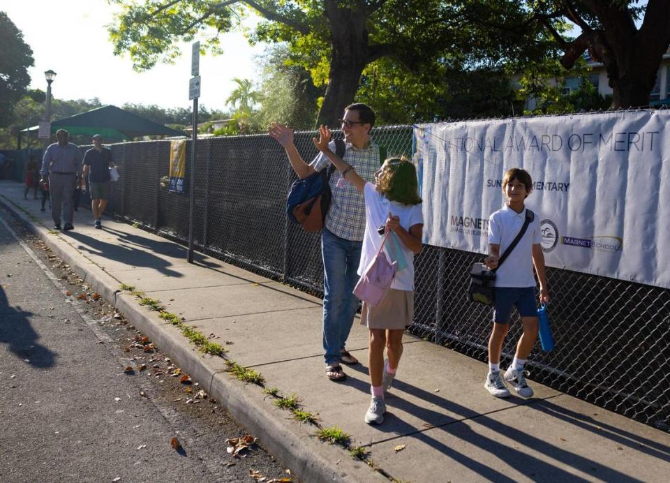 Elena Gonzalez, 10, center, waves while she walks into the first day of school with her father and brother at Sunset Elementary School on Wednesday, Aug. 17, 2022, in Miami.