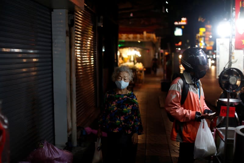 An elderly woman wearing a mask walks past a delivery man at an empty street during the coronavirus disease (COVID-19) outbreak, in Chinatown, Bangkok