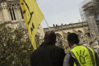 Protesters look at technicians working on top of the Notre Dame cathedral in Paris, Monday, April 22, 2019. In the wake of the fire last week that gutted Notre Dame, questions are being raised about the state of thousands of other cathedrals, palaces and village spires that have turned France — as well as Italy, Britain and Spain — into open air museums of Western civilization. (AP Photo/Francisco Seco)