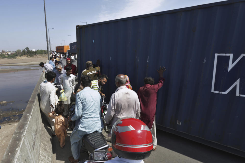 People cross a bridge on Ravi River which is closed for traffic due to shipping containers placed by authorities in an attempt to foil a planned protest of Pakistan's main opposition party, in Lahore, Pakistan, Tuesday, May 24, 2022. Pakistan's key opposition party led by recently ousted Prime Minister Imran Khan accused police of detaining hundreds of its supporters in raids that started early Tuesday. (AP Photo/K.M. Chaudary)