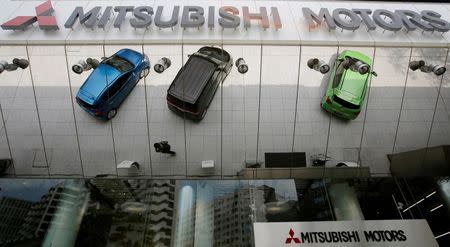 Mitsubishi Motors Corp's vehicles and a passer-by are reflected on an external wall at the company headquarters in Tokyo May 23, 2013. REUTERS/Toru Hanai/File Photo