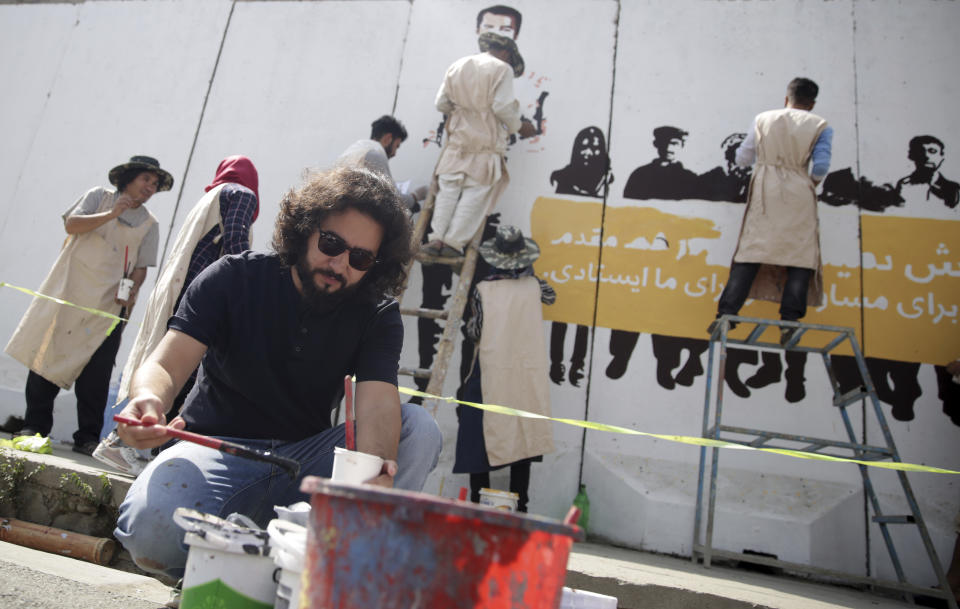 Omaid Sharifi, artist and the head of ArtLords organization, refills the color cup as he and other artists paint a mural of journalists who have been killed during the year of 2018, in Kabul, Afghanistan, Tuesday, Sept. 25, 2018. It's the first in a series of murals planned by Amnesty International and the Artlords collective to highlight the work of Afghan activists, teachers, lawyers, students, trade unionists and others. (AP Photo/Massoud Hossaini)