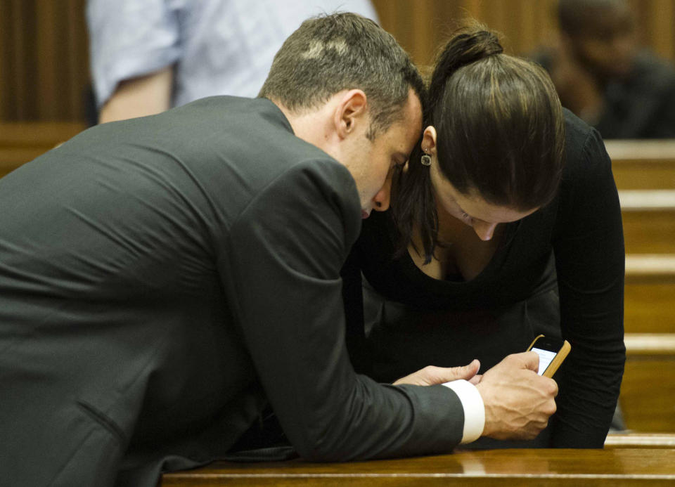 Oscar Pistorius, left, shows his mobile phone to sister Aimee on the fifth day of his trial at the high court in Pretoria, South Africa, Friday, March 7, 2014. Pistorius is charged with murder for the shooting death of his girlfriend, Reeva Steenkamp, on Valentines Day in 2013. (AP Photo/Theana Breugem, Pool)