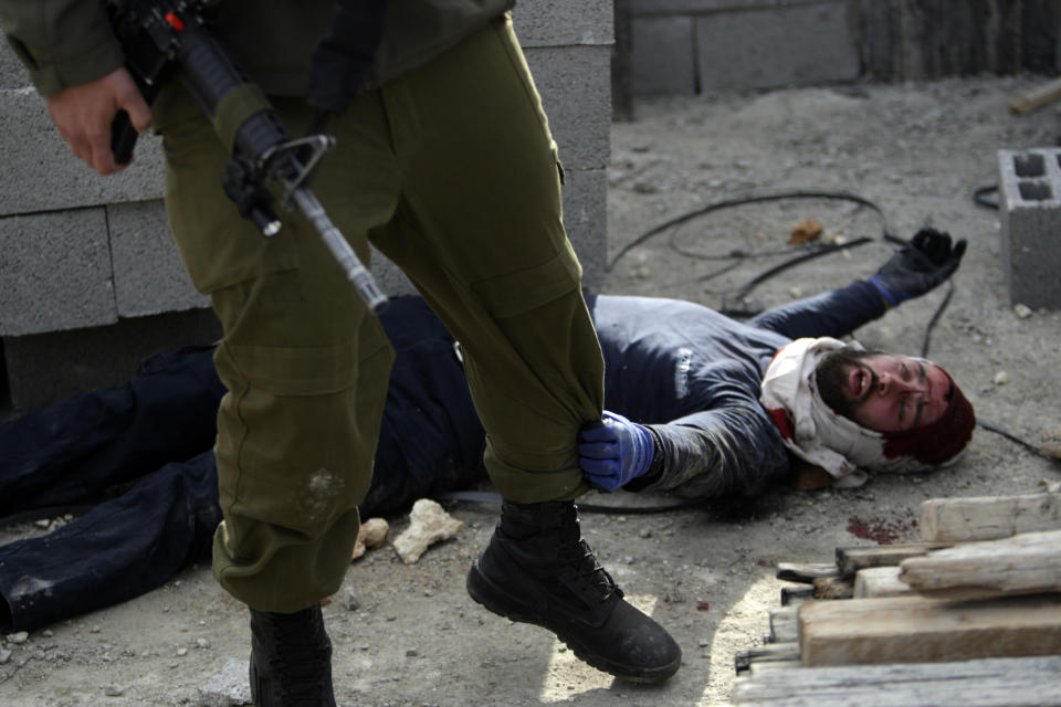 An injured Israeli settler grabs an Israeli soldier's leg to get his attention after the settler was detained by Palestinian villagers in a building under construction near the West Bank village of Qusra, Jan. 7, 2014. (AP Photo/Nasser Ishtayeh)