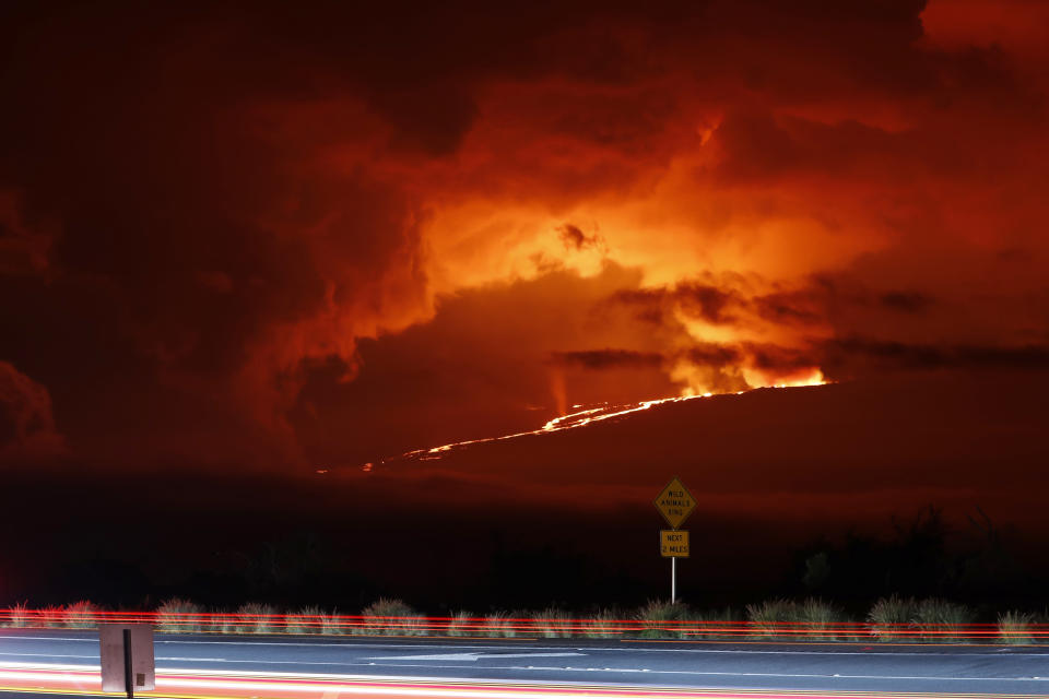 Cars drive down Saddle Road as Mauna Loa erupts in the distance, Monday, Nov. 28, 2022, near Hilo, Hawaii. (AP Photo/Marco Garcia)