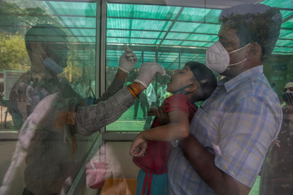 A health worker takes a swab sample of a child to test for COVID-19 at a government hospital in Noida, a suburb of New Delhi, India, Thursday, April 15, 2021. India reported more than 200,000 new coronavirus cases Thursday, skyrocketing past 14 million overall as an intensifying outbreak puts a grim weight on its fragile health care system. (AP Photo/Altaf Qadri)