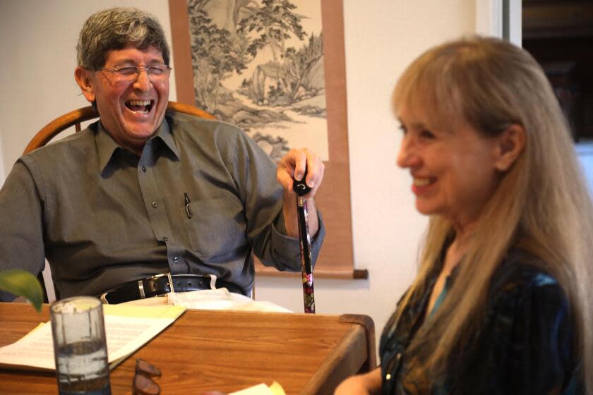 SANTA CLARITA, CA - APRIL 9, 2024 - - Geriatrician Dr. Gene Dorio, left, and life partner Robin Clough enjoy a light moment in the kitchen of their home in Santa Clarita on April 9, 2024. Dr. Dorio, who mostly does house calls with senior patients, has been spending most of his time taking care of Clough who has been battling papillary carcinoma cancer. After weeks of cancer treatment Clough is currently diagnosed "no cancer determined/no evidence of cancer." "To me it's like bonus days," Clough said about her recent cancer diagnosis. "I was suppose to be gone," she concluded. (Genaro Molina/Los Angeles Times)