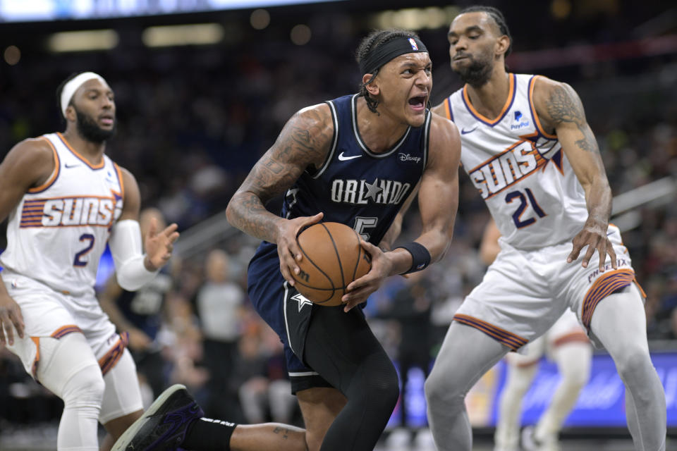 Orlando Magic forward Paolo Banchero (5) drives to the basket while defended by Phoenix Suns forward Keita Bates-Diop (21) as Suns' Josh Okogie (2) looks on during the first half of an NBA basketball game, Sunday, Jan. 28, 2024, in Orlando, Fla. (AP Photo/Phelan M. Ebenhack)