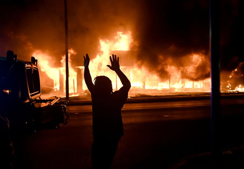 Un hombre camina al lado de un vehículo blindado mientras B&L Office Furniture se quema en el fondo después de protestas que terminaron en incendios luego de que la policía disparó varias veces a un hombre negro, identificado como Jacob Blake, anoche en Kenosha, Wisconsin, Estados Unidos.