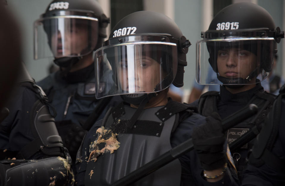 A police officer stands her ground after protesters threw food at officers, as police block them from reaching La Fortaleza governor's residence in San Juan, Puerto Rico, Sunday, July 14, 2019. Protesters are demanding Gov. Ricardo Rosselló step down for his involvement in a private chat in which he used profanities to describe an ex-New York City councilwoman and a federal control board overseeing the island's finance. (AP Photo/Carlos Giusti)