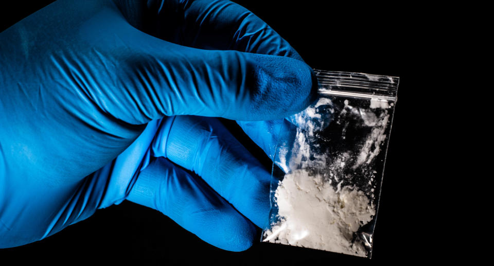 A gloved hand holding a small bag of white powder.