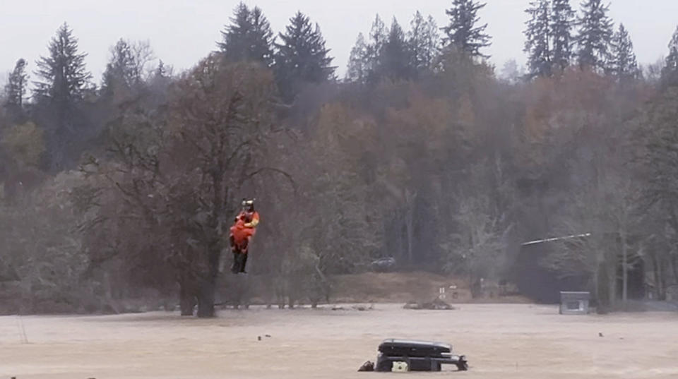 In this still from a video provided by Nicole Langer, a woman is rescued by a U.S. Coast Guard officer from a flooded truck in Grays River, Washington, on Tuesday, Nov. 5, 2023. According to Langer, the woman tried to drive on flooded roads. The Coast Guard aircrew also rescued four other people nearby trapped on top of their house. An atmospheric river brought heavy rain, flooding and unseasonably warm temperatures to the Pacific Northwest. (Nicole Langer via AP)