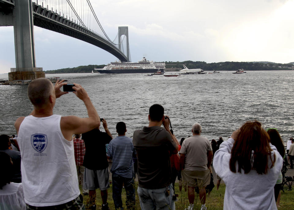 People gather to watch and take pictures as the space shuttle Enterprise is towed on a barge underneath the Verrazano-Narrows Bridge in New York, Sunday, June 3, 2012. The prototype space shuttle that arrived in New York City earlier this spring is headed to the Intrepid Sea, Air and Space Museum on the west side of Manhattan. (AP Photo/Seth Wenig)