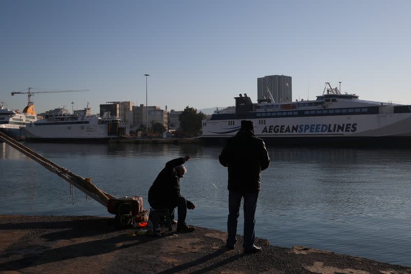 People fish as passenger ferries are moored during a 24-hour strike at the Port of Piraeus, near Athens