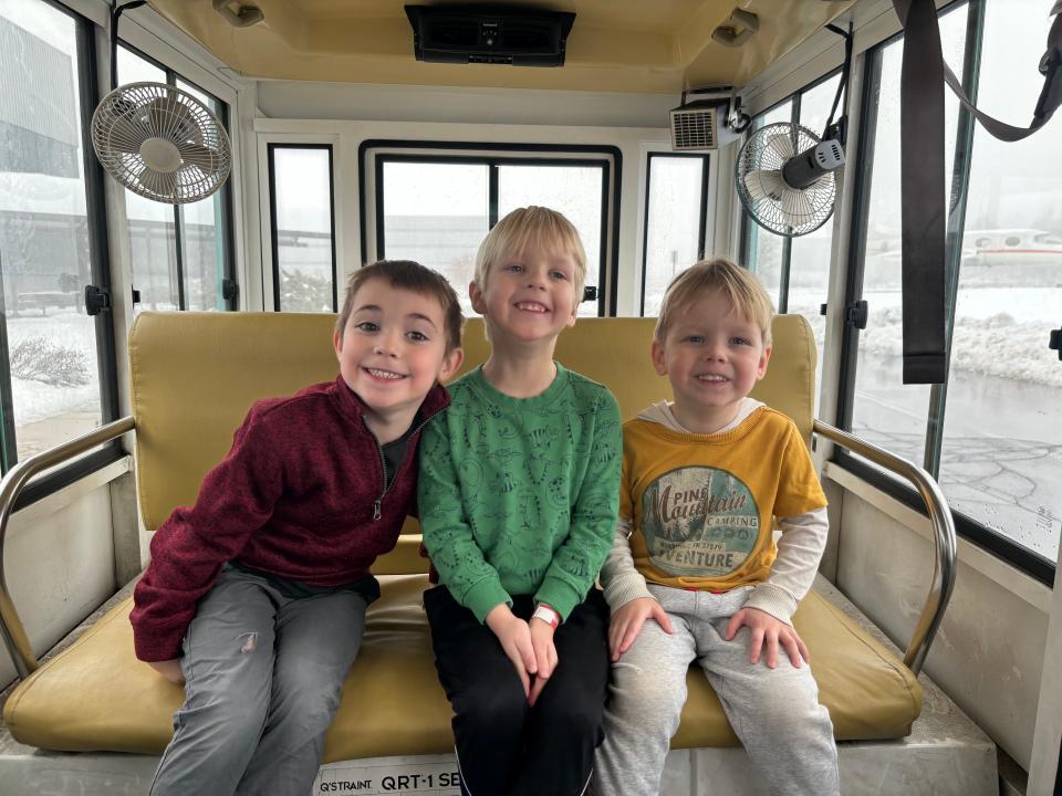 Three boys smiling and looking at the camera sitting and looking in a vehicle.