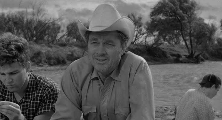 Three people outdoors with a vintage look; a man in a cowboy hat is center focus