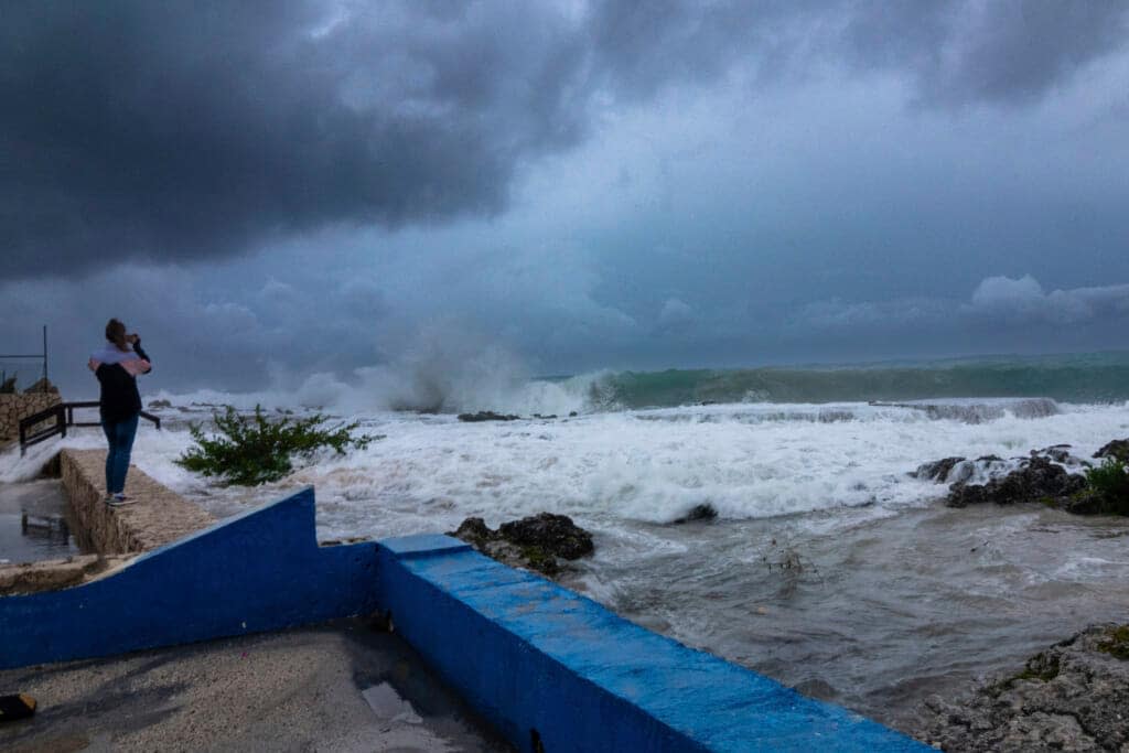 A woman takes photos while waves crash against a seawall as Hurricane Ian passes through George Town, Grand Cayman island, Sept. 26, 2022. Hurricane Ian is quickly gaining monstrous strength as it moves over oceans partly heated up by climate change. (AP Photo/Kevin Morales, File)