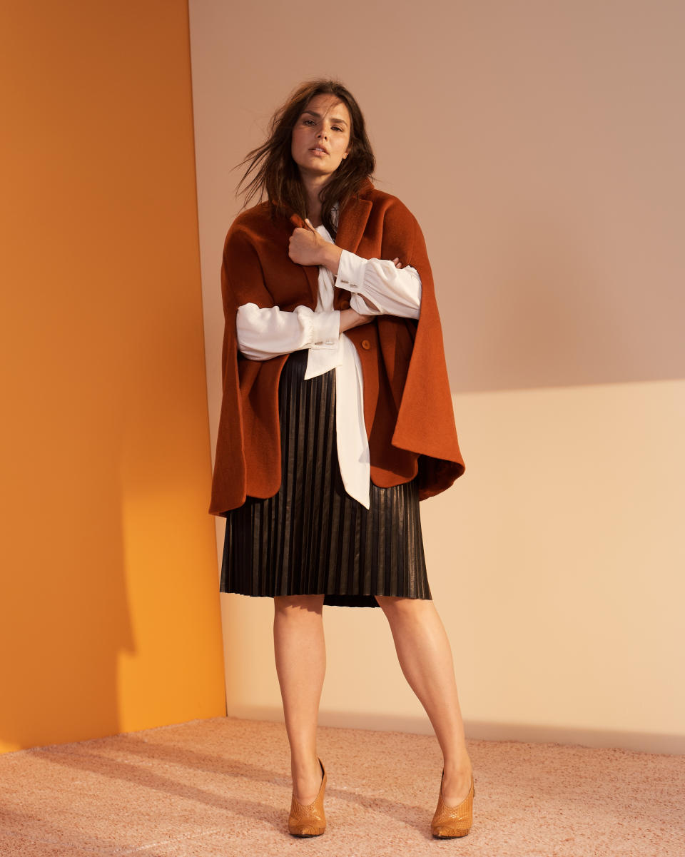 Candice Huffine wears a burnt-orange cape, white blouse, and black pleated skirt from the new Prabal Gurung x Lane Bryant collection. (Photo: Courtesy of Lane Bryant)