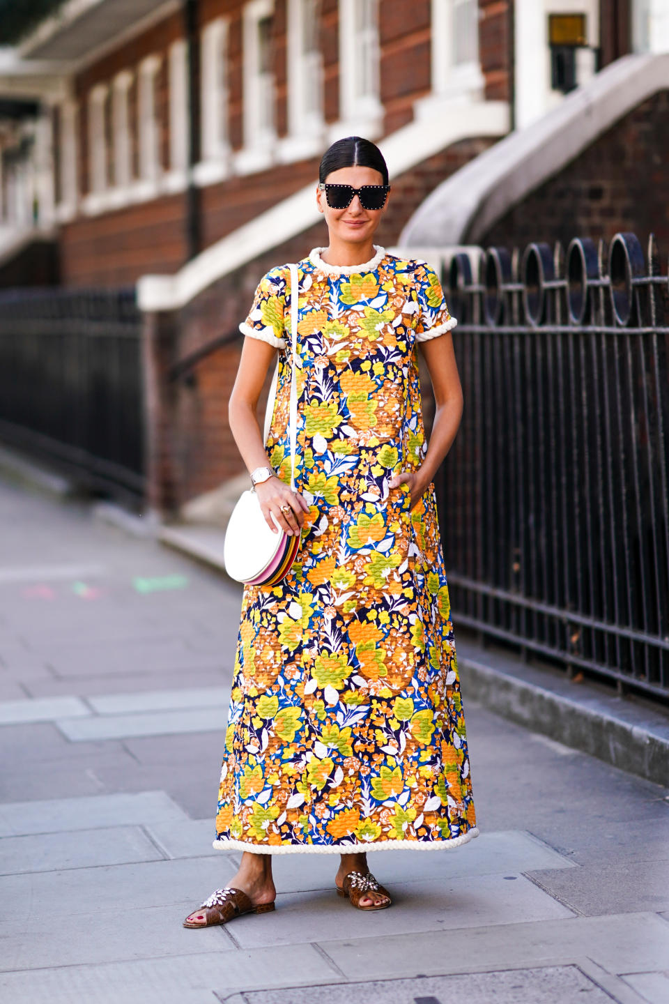 Giovanna Battaglia is seen wearing a coloured floral print dress, sunglasses, a bag, brown sandals. [Photo: Getty Images]