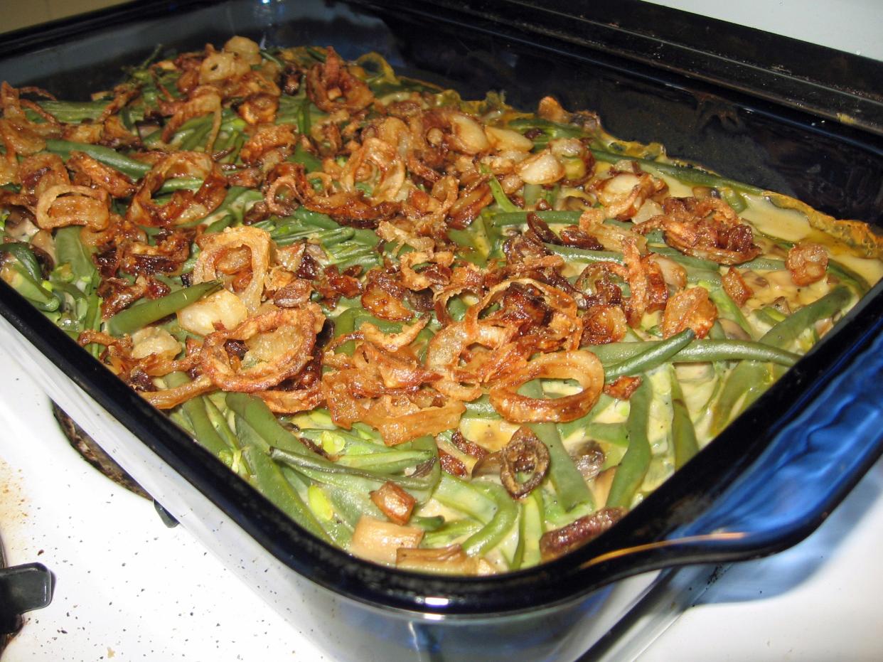 Green bean casserole with bechamel and homemade onion rings in a rectangular clear glass baking dish.