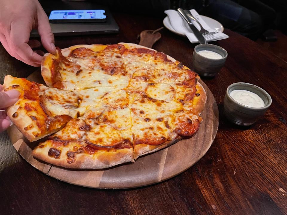 Hands taking slices of a cheese pizza away on a wooden table