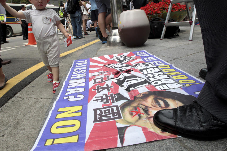 FILE - A protester steps on a portrait of Japanese Prime Minister Shinzo Abe and the Rising Sun flag during an anti-Japan rally in front of the Japanese embassy in Seoul, South Korea on July 2, 2014. Japan’s longest-serving prime minister, Shinzo Abe was credited with instilling political and economic stability. However, he angered Japan’s neighbors South Korea and China along with many Japanese with his nationalistic rhetoric and calls to revise the country’s pacifist constitution. (AP Photo/Ahn Young-joon, File)