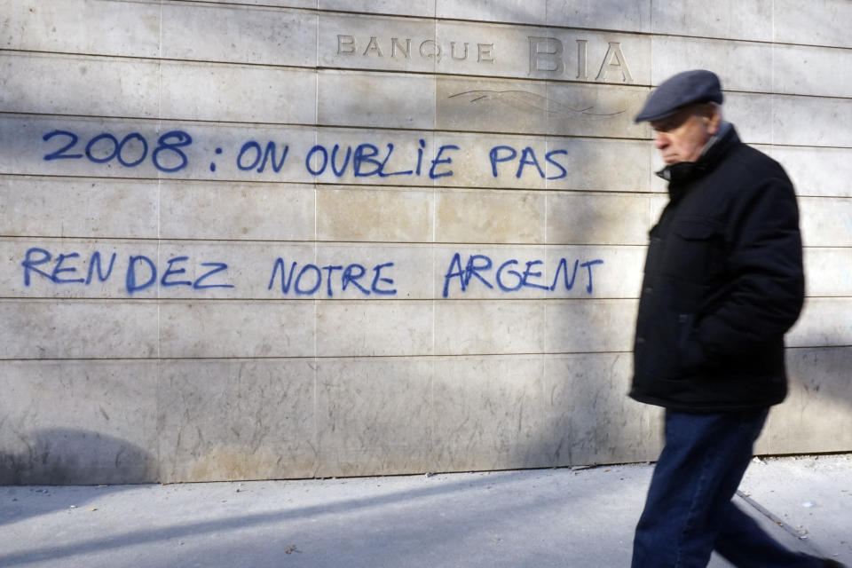 In this photo taken on Thursday, Dec. 13, 2018, a man walks past French graffiti that reads: "2008: We haven't forgotten, Give us back our money", a few blocks from the Champs Elysees in Paris. Across the world, people are questioning truths they had long held to be self-evident, and they are dismissing some of them as fake news. They are replacing traditions they had long seen as immutable with haphazard reinvention. In France, people who feel left behind by a globalizing world have spent the last few weeks marching and rioting to protest a government they call elitist and out of touch. (AP Photo/Raphael Satter)