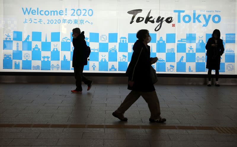 Man wearing a protective mask in front of an advertising billboard of Tokyo Olympics 2020, near the Shinjuku station in Tokyo