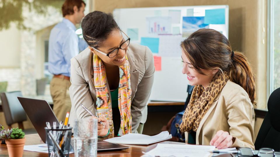 Cheerful mid adult African American and young Caucasian businesswomen discuss something in the office.