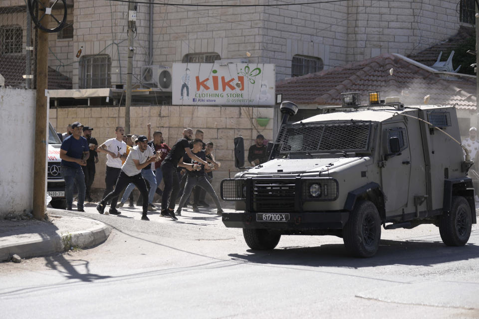 Palestinians throw stones at an Israeli military vehicle following a deadly raid in the occupied West Bank town of Jenin, Wednesday, Sept. 28, 2022. At least four Palestinians were killed and dozens of others wounded, the Palestinian Health Ministry reported, the latest in a series of deadly Israeli operations in the occupied territory. (AP Photo/ Majdi Mohammed)