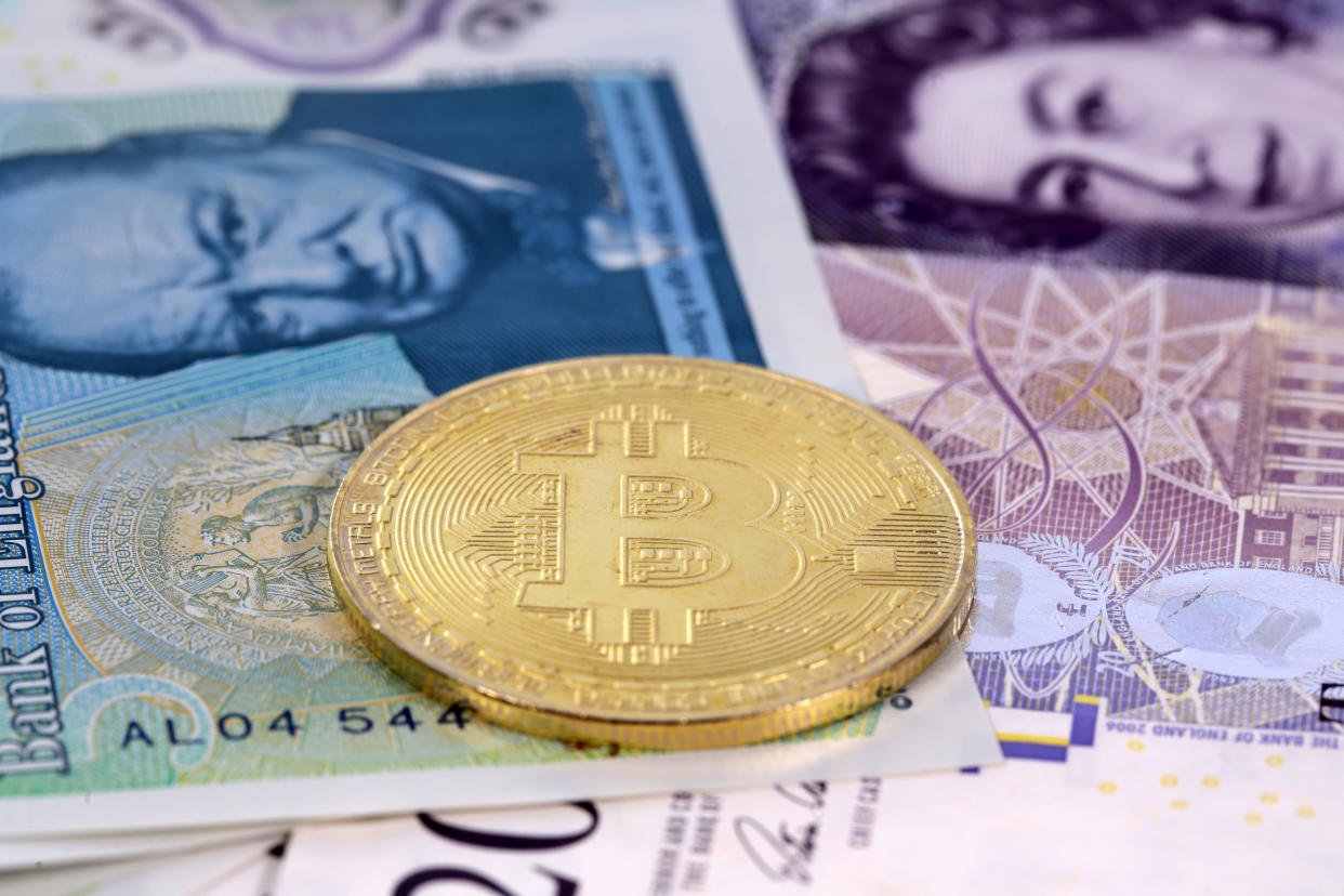 Single virtual cryptocurrency money Bitcoin golden coin on United Kingdom Pound sterling banknotes with faces of Queen Elizabeth II and Winston Churchill.