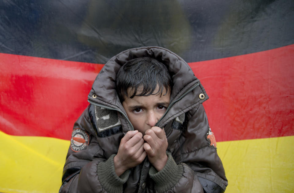 FILE - In this Wednesday, March 9, 2016 file photo a child tries to warm his hands, backdropped by Germany's flag as protesting migrants stage a sit in protest on the railway tracks at northern Greek border station of Idomeni. A new study estimates that at least 3.9 million unauthorized migrants, and possibly as many as 4.8 million, lived in Europe in 2017 with half of them in Germany and the United Kingdom. (AP Photo/Vadim Ghirda, file)