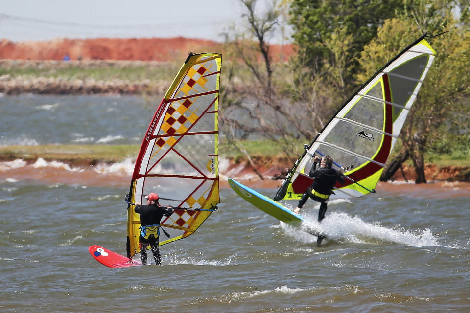 In this April 27, 2020, photo, windsurfers head out from shore on Lake Hefner in Oklahoma City. From Cape Cod to California, festivals are being canceled, businesses in tourist havens are looking at empty reservation books, and people who have been cooped up through a dismal spring are worrying summer will bring just more of the same. (AP Photo/Sue Ogrocki, File)