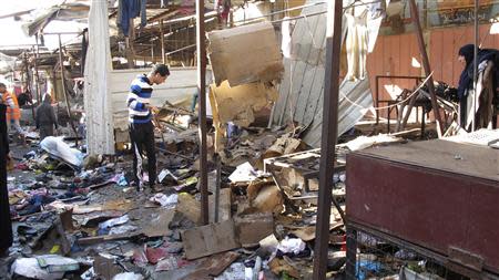 People stand among debris at the site of a bomb attack at a marketplace in Baghdad's Doura District December 25, 2013. REUTERS/Ahmed Malik