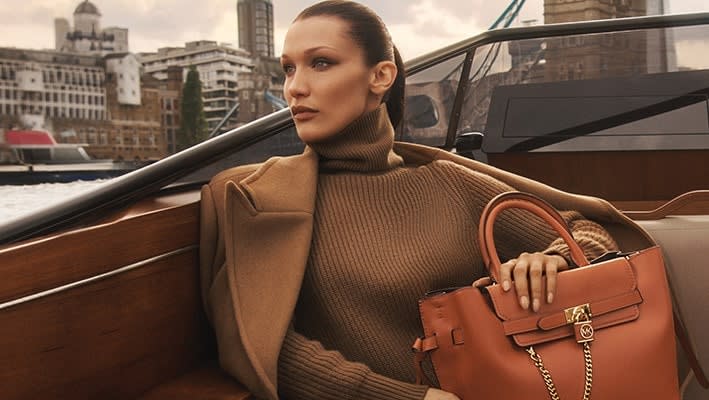  A model sits on a luxury boat cruising down the river of a city with a Michael Kors handbag on her arm 