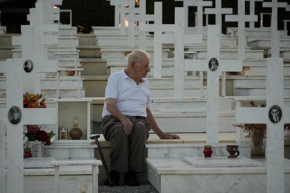 Loucas Alexandrou, de 94 años, sentado en la tumba de su hijo, Christakis Alexandrou, Alexandrides, fallecido el 22 de julio de 1974 durante la invasión turca, en el cementerio militar de la dividida capital de Chipre, Nicosia, el 19 de julio de 2024. (AP Foto/Petros Karadjias)