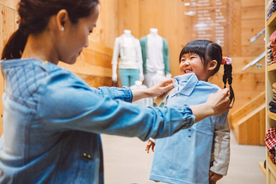 A woman holds up a shirt to her daughter to see how it might fit and look on her