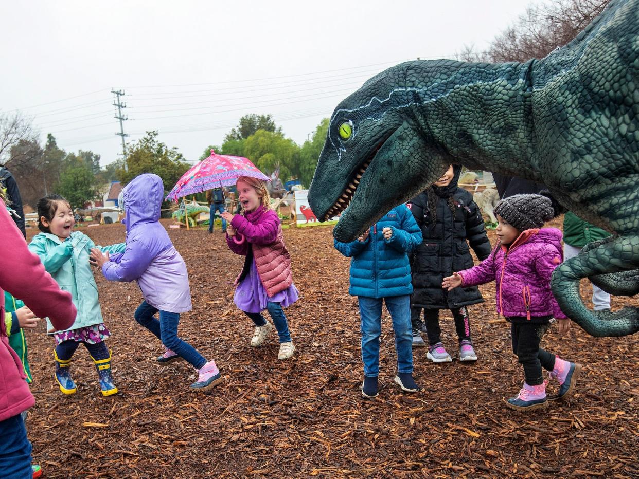 Children playing in wet weather clothes near a replica of a velociraptor.