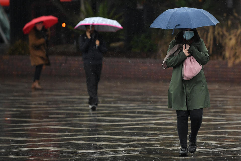 A woman wearing a face mask shelters from the rain during wet weather at Circular Quay in Sydney, Sunday, July 26, 2020