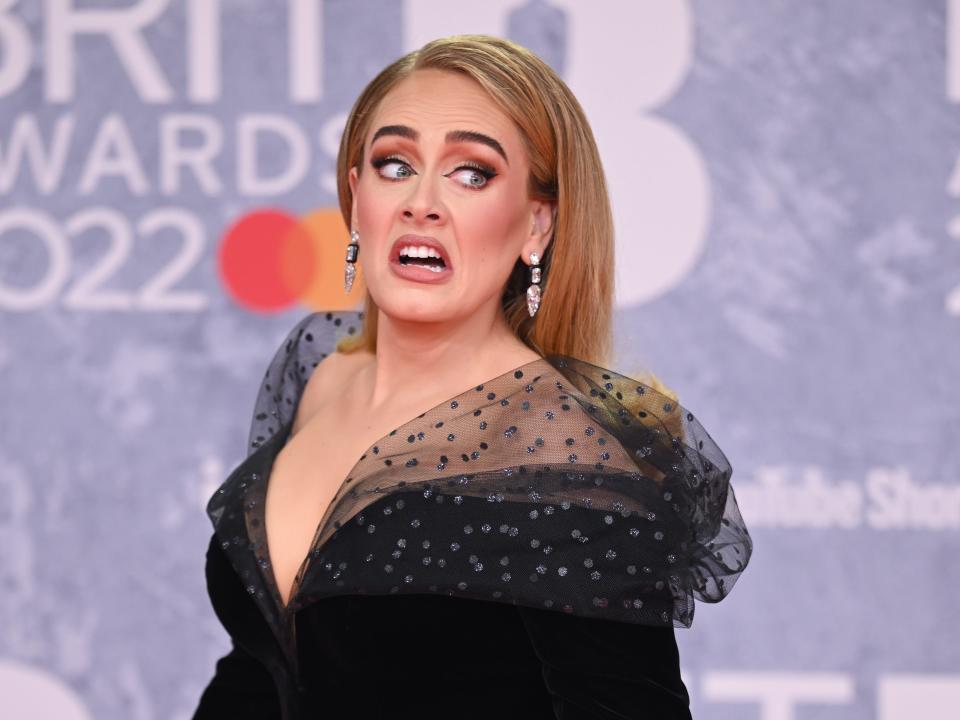 Adele looking back with a worried or surprised face with her mouth open. She's wearing a black off the shoulder gown.