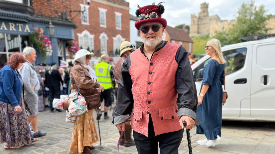 Man dressed in red-speckled waistcoat with a red top hat and goggles