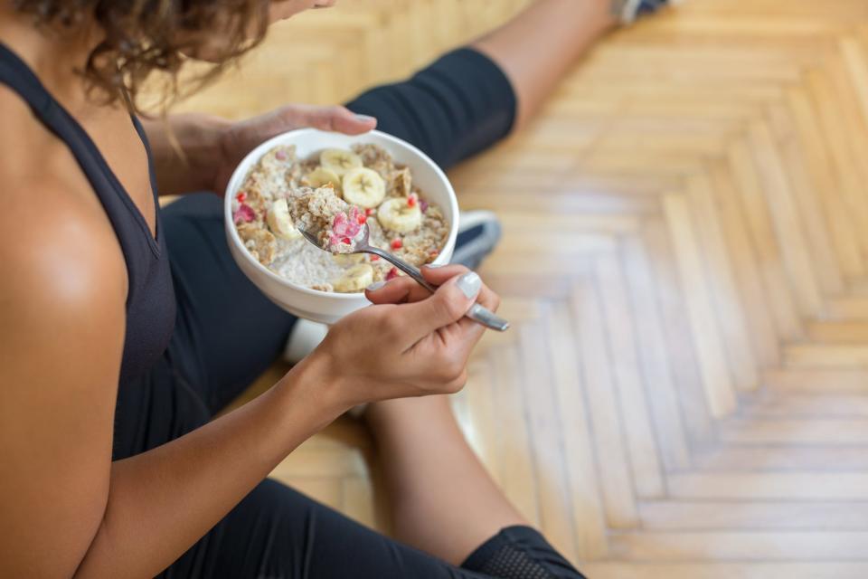 An top down view of a woman in gym clothes eating oatmeal with fruit after a workout.