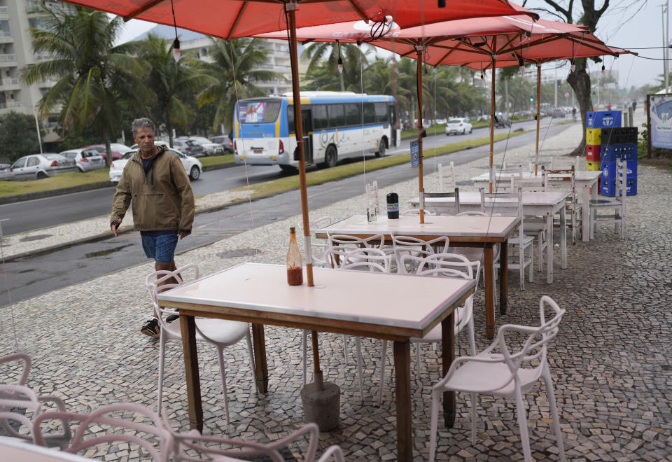 A pedestrian walks past the table, front, where four doctors were sitting when they were shot at the food and bar kiosk "Nana 2" on the beach in the Barra de Tijuca neighborhood of Rio de Janeiro, Brazil, Thursday, Oct. 5, 2023. Three of the doctors died in the overnight shooting. (AP Photo/Silvia Izquierdo)