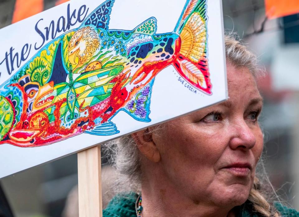 Sue Coccia holds a sign the she designed as she marches through downtown Tacoma to advocate for the removal of the Snake River dams and rally against the extinction of protected salmon in March 2022.