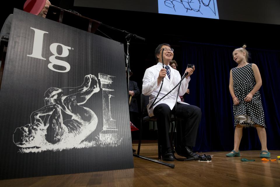 Akira Horiuchi, center, of Japan, who won the Ig Nobel in medical education demonstrates his self colonoscopy technic as Miss Sweetie Poo, right, attempts to cut him off for going over his allotted time during award ceremonies at Harvard University in Cambridge, Mass., Thursday, Sept. 13, 2018.(AP Photo/Michael Dwyer)