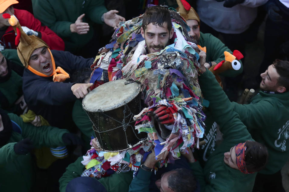 In this photo taken on Sunday, Jan. 19, 2020, a man is lifted by people after playing the Jarramplas in the Spanish town of Piornal, Spain. The Jarramplas festival features a man in multicolored garb and pointy wooden headgear to shield himself from turnips. A crowd of men in the street pelt the man with the vegetables from close range at the fiesta held annually at Piornal, 200 kilometers west of Madrid, over two days. (AP Photo/Manu Fernandez)