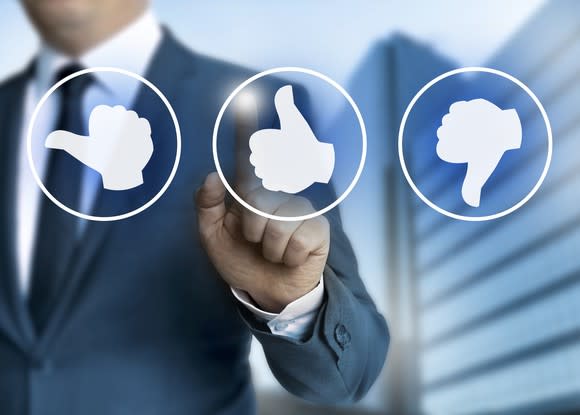 A businessman in a suit points at a thumbs up icon floating in front of him.